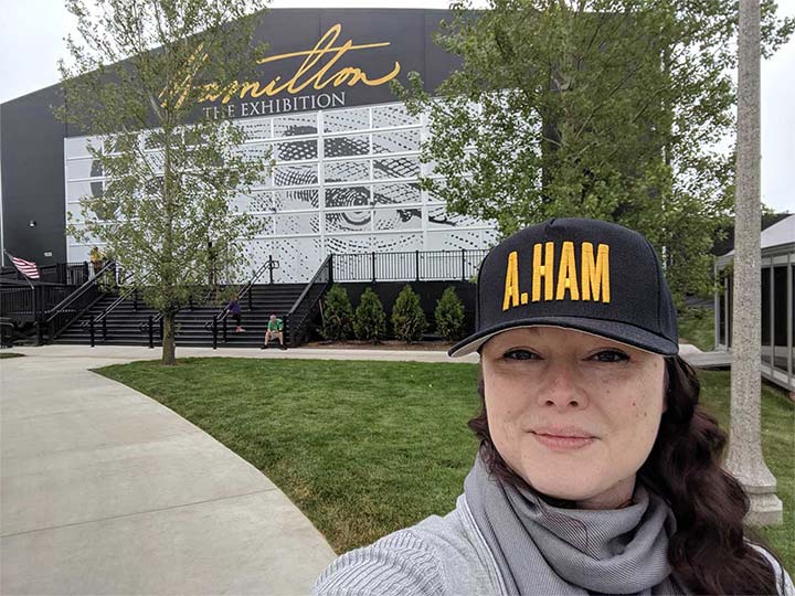 Rachael Cristine Woody stands outside Hamilton: The Exhibition wearing the iconic A. Ham baseball hat.