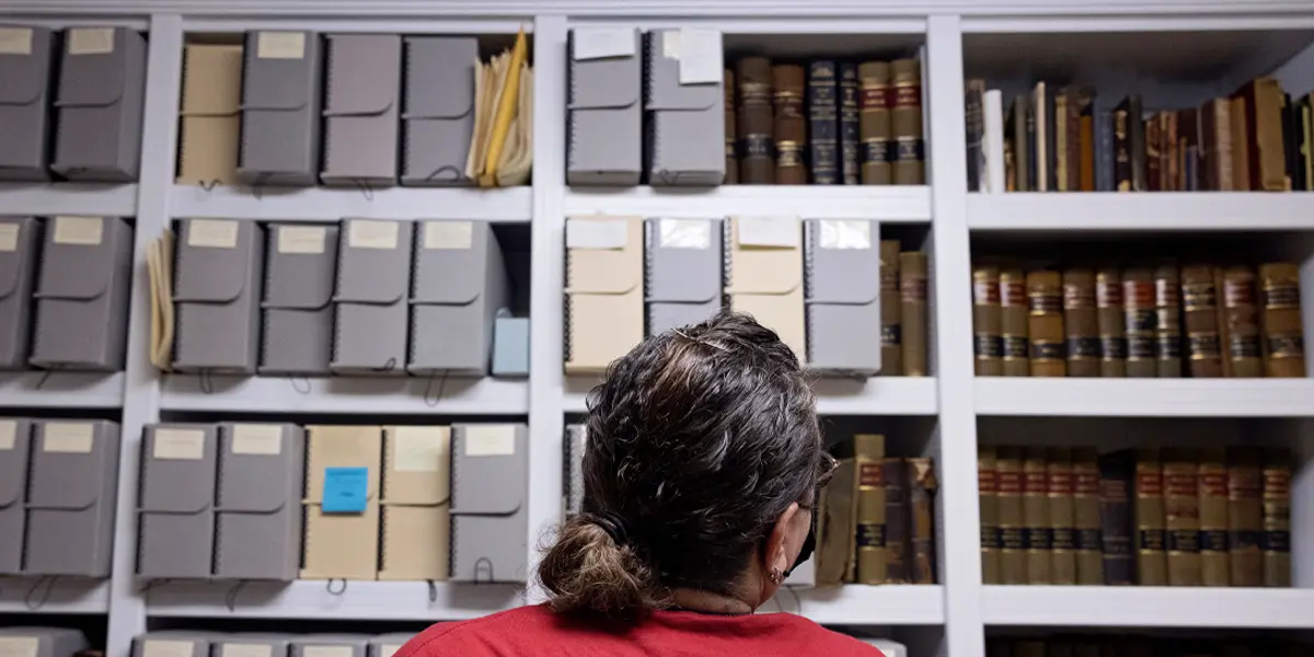 Woman at a university archive looking at shelf full of archival boxes and books