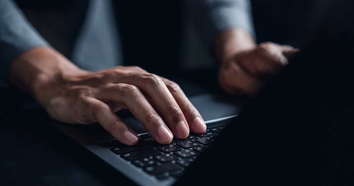 Cover image: A person types on a laptop keyboard with focus and intensity. The scene is dimly lit, highlighting the hands and creating a professional tone.