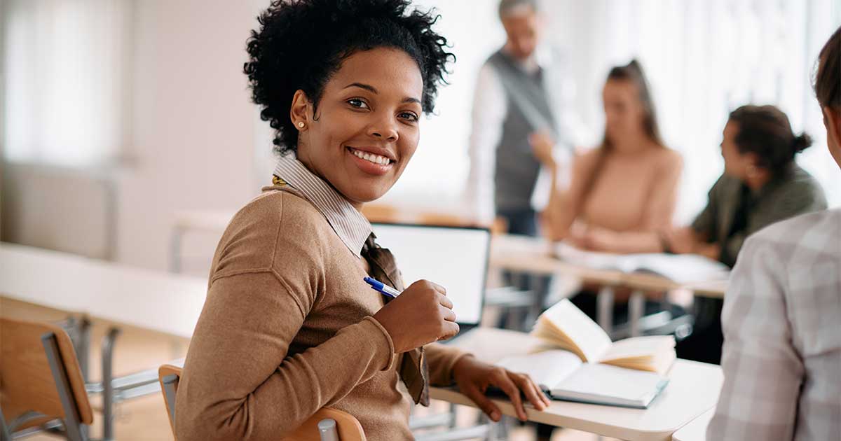 Cover image for Active Learning in Library Instruction, by Lauren Hays featuring a smiling woman with curly hair holds a pen and book in a classroom. Other people in the background are engaged in discussion, creating a collaborative learning atmosphere.