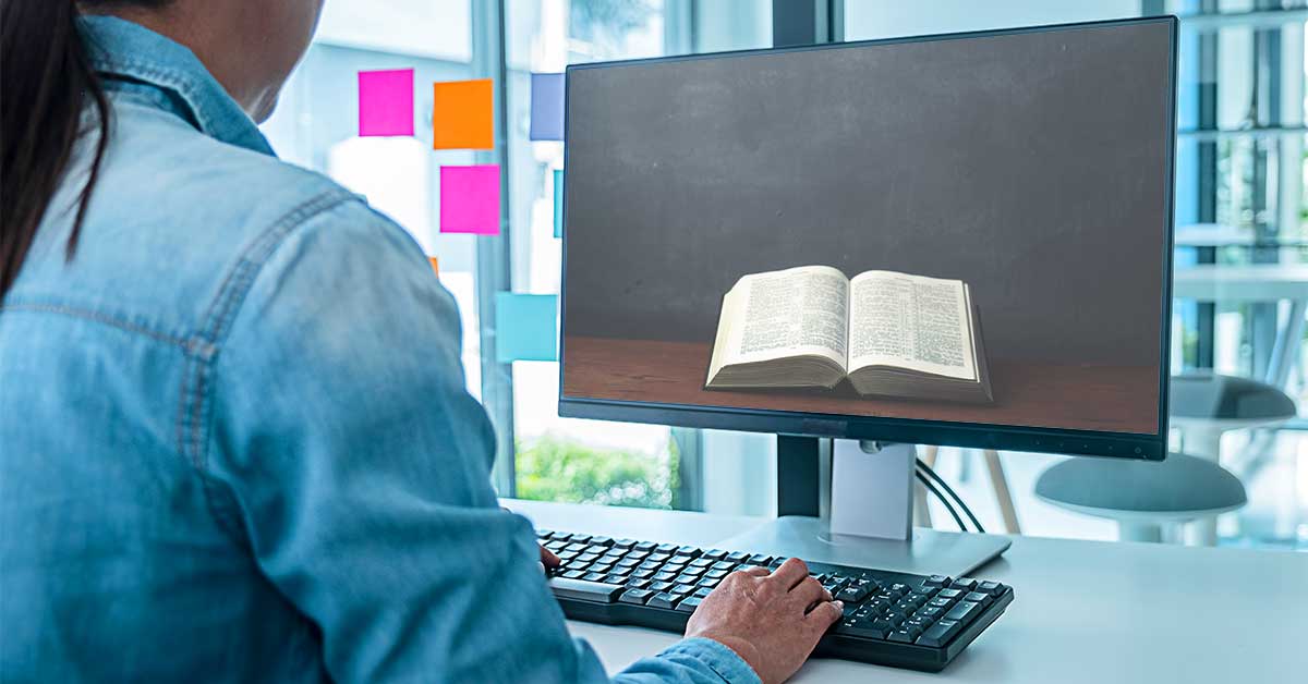 A person wearing a denim shirt views an open dictionary on a computer screen, surrounded by colorful sticky notes on a window. The scene is professional and modern.