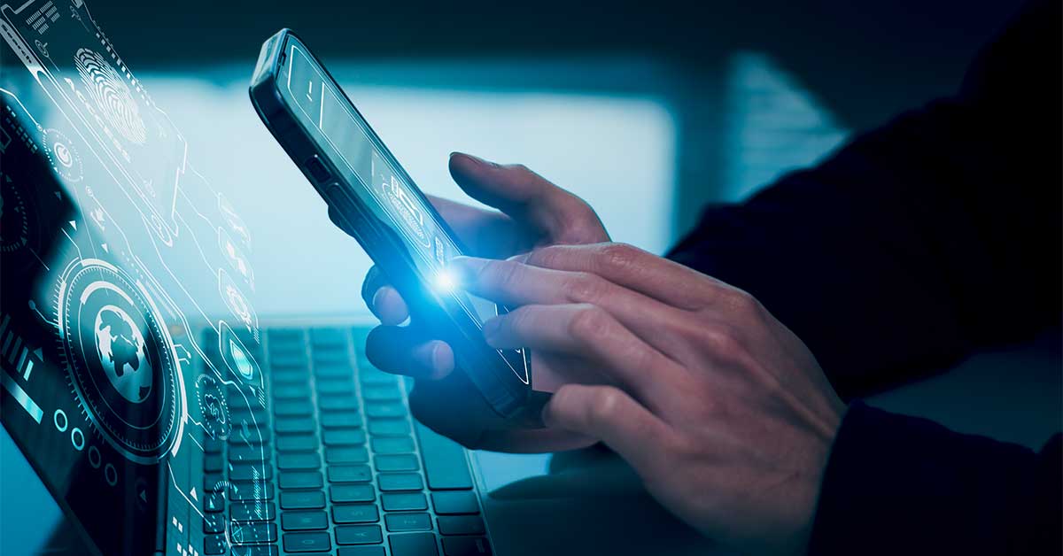 A person using their smartphone in front of a laptop.