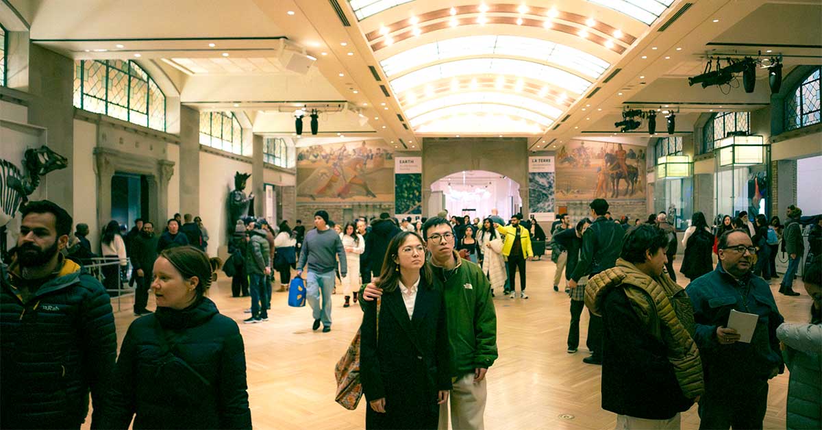 A crowd of people walking through a brightly lit a museum atrium.