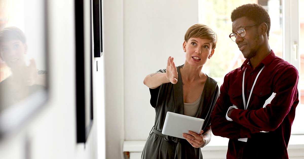 Two museum workers discussing a wall of art, representing the Adopt-an-Artifact programs offered by entrepreneurial museums.