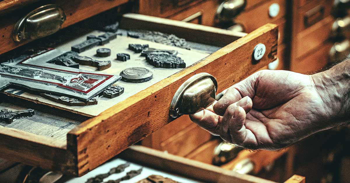 A museum worker pulling open a drawer filled with small metal artifacts.