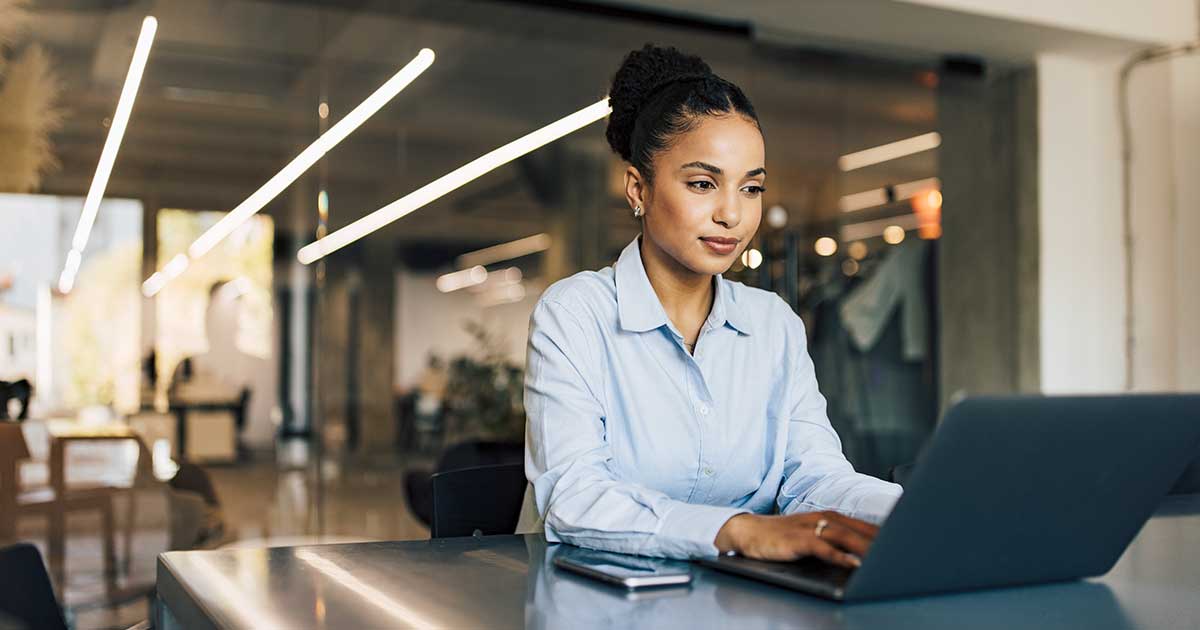 A professional settling in at a new workplace, typing on a laptop at a desk in a bright, open office.