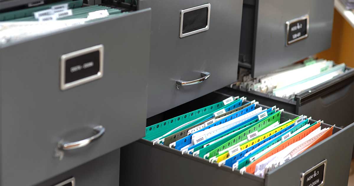 Open filing cabinet drawers filled with color-coded hanging folders, each tab labeled with a record number.