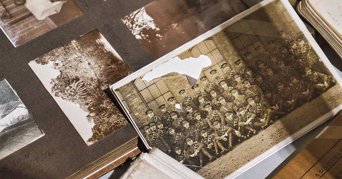 Faded sepia group photograph of uniformed soldiers, its top corner torn, resting on an open album of mounted historical photographs.